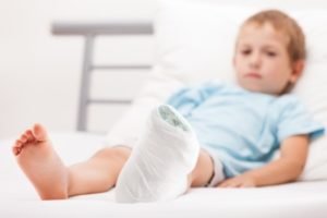 An injured child sat on a hospital bed with a bandaged foot.