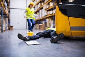 A worker inside a warehouse helps an injured colleague lying on the floor