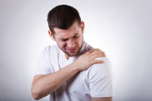 A man in a white shirt grimaces in pain as he holds his shoulder