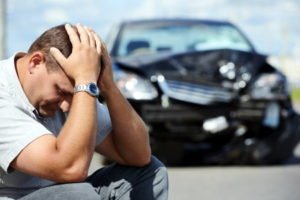 A kneeling man holds his head following a car accident. 