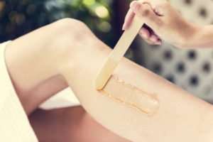 A person receiving waxing treatment on one of their legs