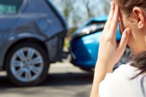 Passenger injured in road traffic accident sat by the side of two blue cars.