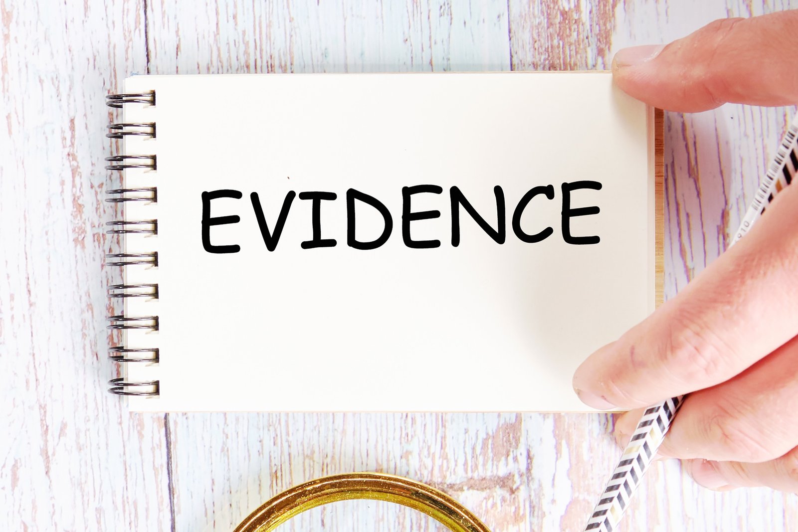 A Hand Holds A Notebook With Evidence Written On It.