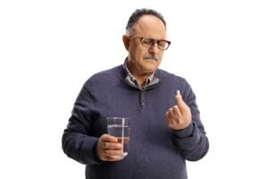 A man holds a pill while holding a glass of water