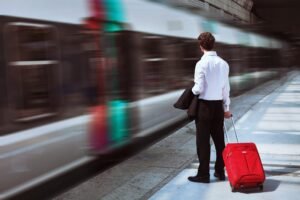 A person standing on a platform and holding a red carry case while a train passes.