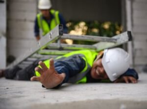 injured construction worker lying on floor with ladder fallen on top of him