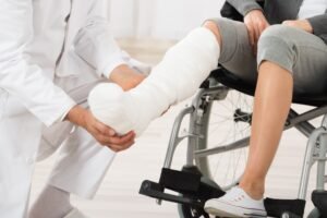 A person in a wheelchair with their foot and toes wrapped in a cast due to an injury while a doctor tends to them. 