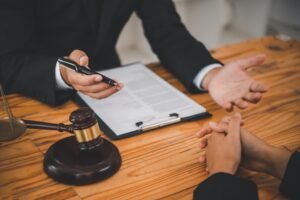 A personal injury solicitor sits behind a wood desk and holds a pen in one hand.