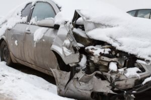 A heavily damaged grey car is covered in snow.