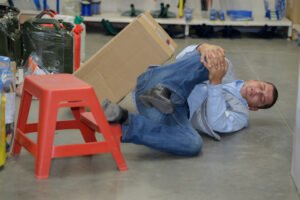 A man holds his knee on the ground after being injured in a workplace accident.