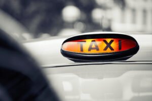 A taxi sign shows on the top of a black cab