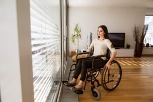 A paralysed woman in a wheelchair looks out of a window.