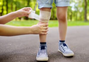 Someone putting a bandage on a child's knee in a park.