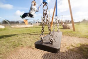 A close-up shot of an empty swing, with children on the other swings in the background. 