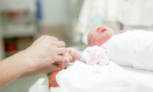 A person holding the hand of a new born baby in hospital after child birth during which the baby suffered medical negligence 