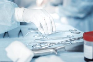 A surgeon picking up a pair of surgery scissors wearing white gloves and scrubs.