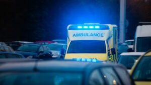 An ambulance with blue lights in the middle of traffic. 