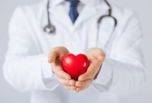 A doctor with a stethoscope around his neck holding a heart figure in his hands.