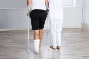 A doctor helping a woman walk with crutches after sustaining a leg hairline fracture 