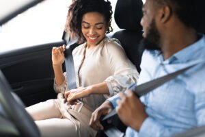 A passenger smiles as she puts on het seatbelt while sitting next to the driver