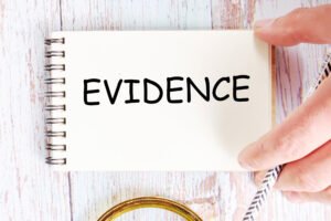 a hand picks up a notebook with the word evidence printed on it on an off-white/wooden background