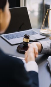 Wrist injury claims solicitor and client share an awkward handshake across a desk with a laptop and gavel on it. 