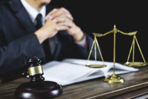 A personal injury team helps a client to make a neck injury compensation claim at a wooden desk with a gavel and scales and open book. 