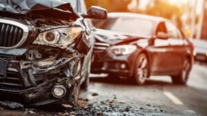 A black car that has sustained severe damage to its bonnet and headlight with another black car that has crashed into the back of it.