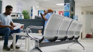 A man in a hospital waiting room with two nurses discussing a file at the reception desk