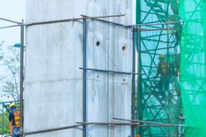 A large concrete pillar and a scaffolding site with netting for safety